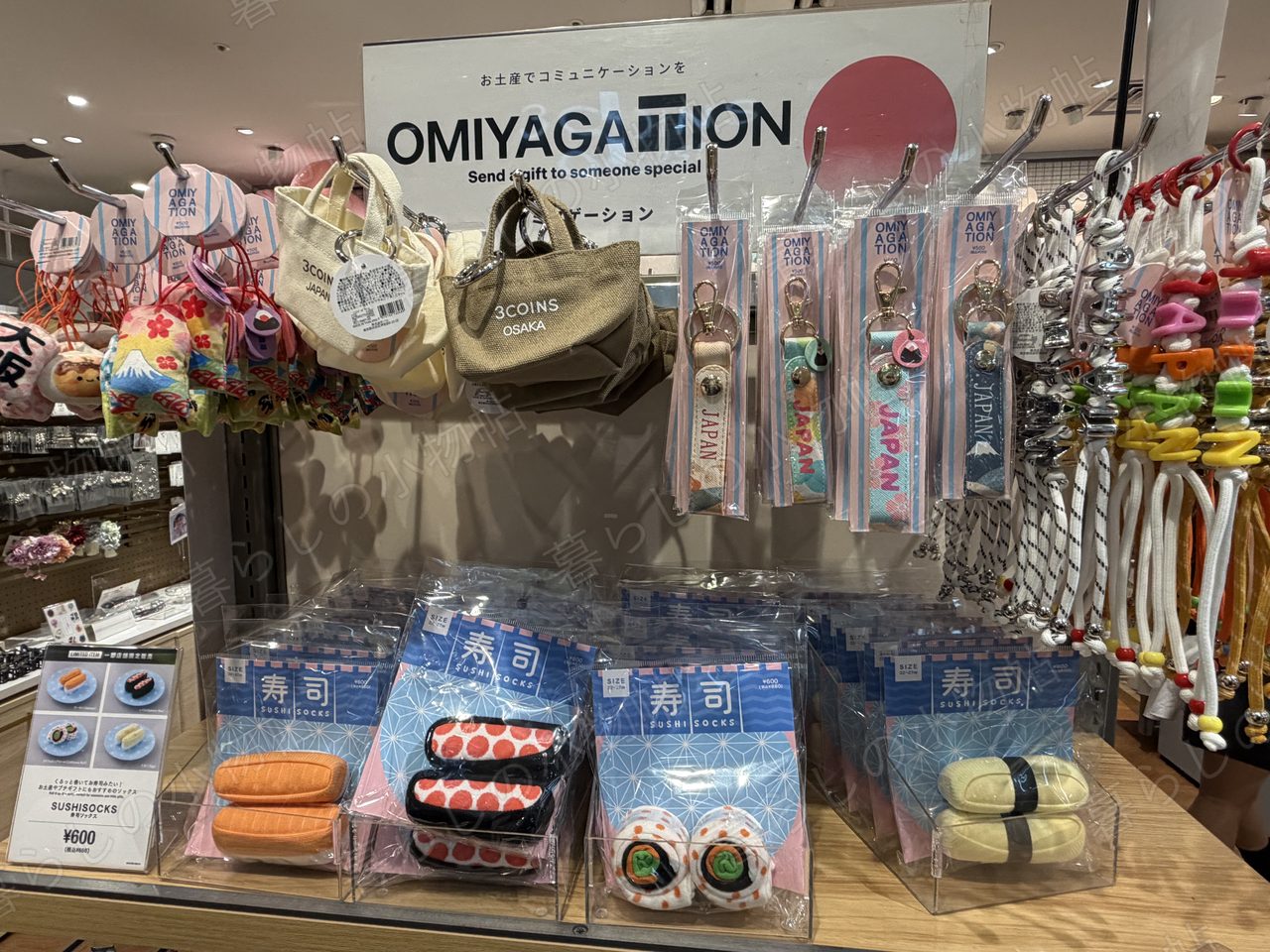 3COINSのOMIYAGATIONコーナー。JAPANキーホルダーや寿司モチーフの靴下が並ぶ棚を撮影