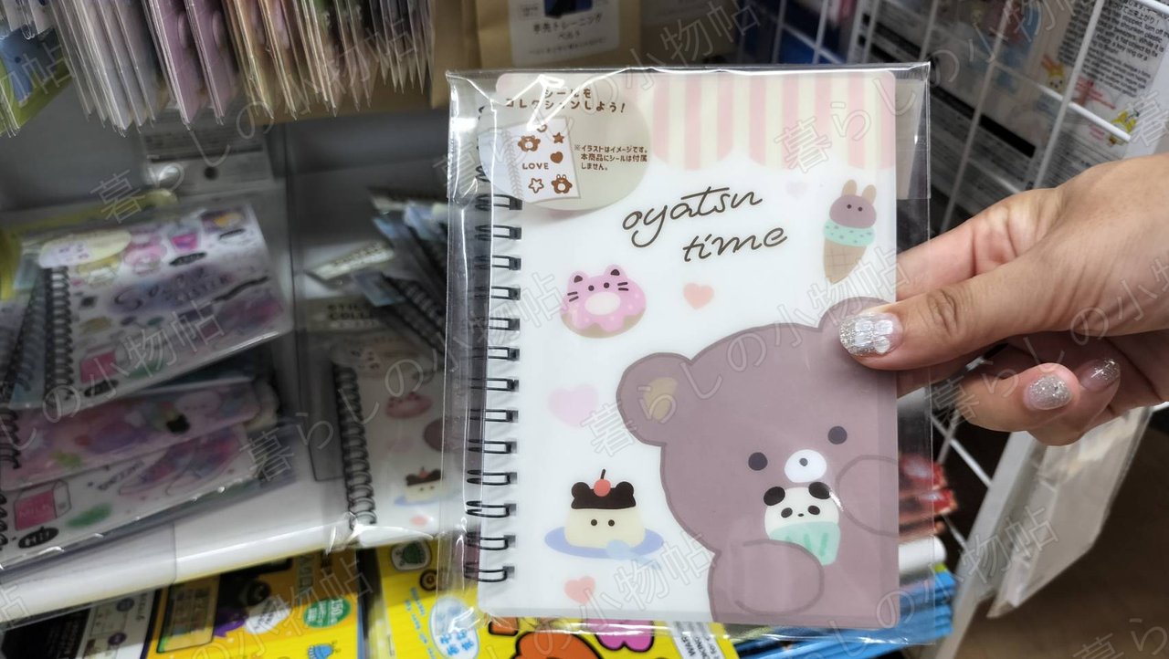 くまとおやつのイラストが描かれたリングタイプのシール帳の表紙を手に持ったところ