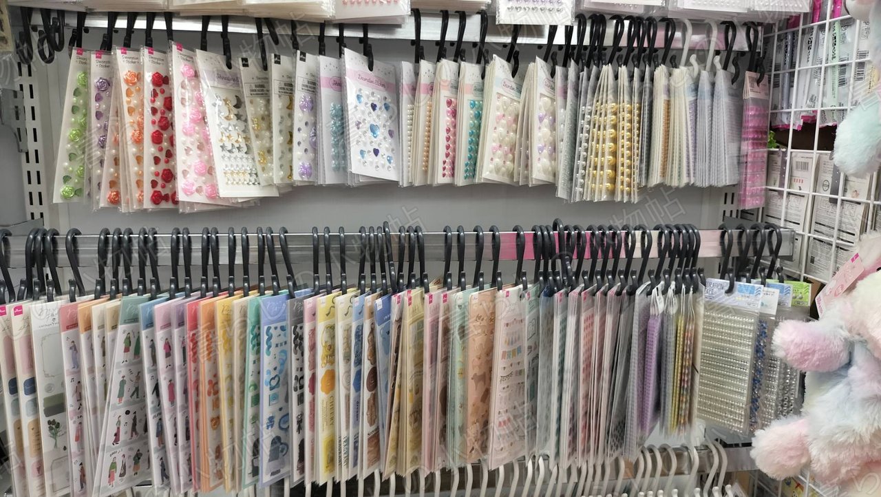 100円ショップのデコレーションシール売り場。パールやフラワーモチーフのシールが壁一面に掛かっている
