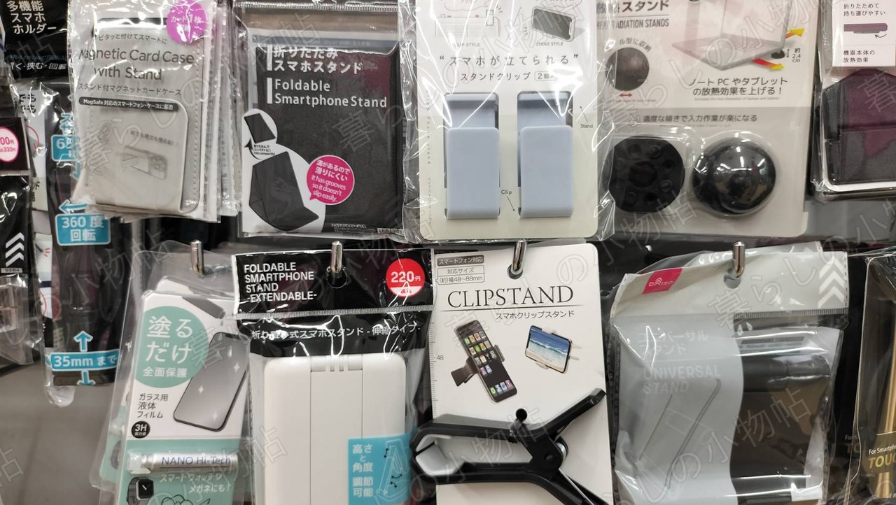 100円ショップのスマホスタンド売り場。折りたたみ式やクリップ式などさまざまなタイプが並んでいる